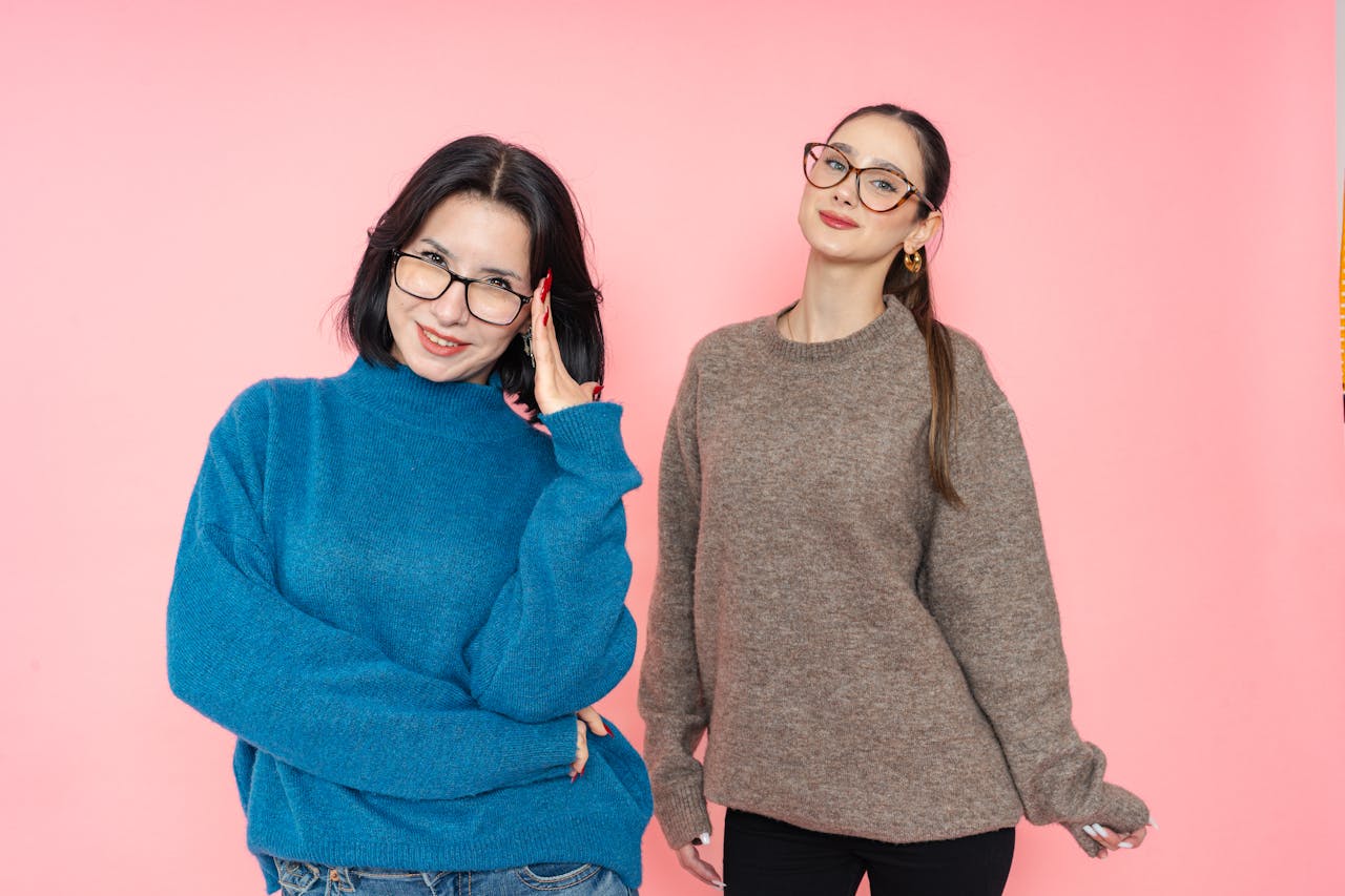 our-story-01 Two women in stylish sweaters posing against a pink background.